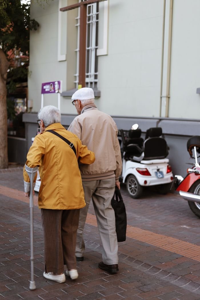 services-03 Senior couple walking together outdoors, one using a cane, showcasing companionship and support.