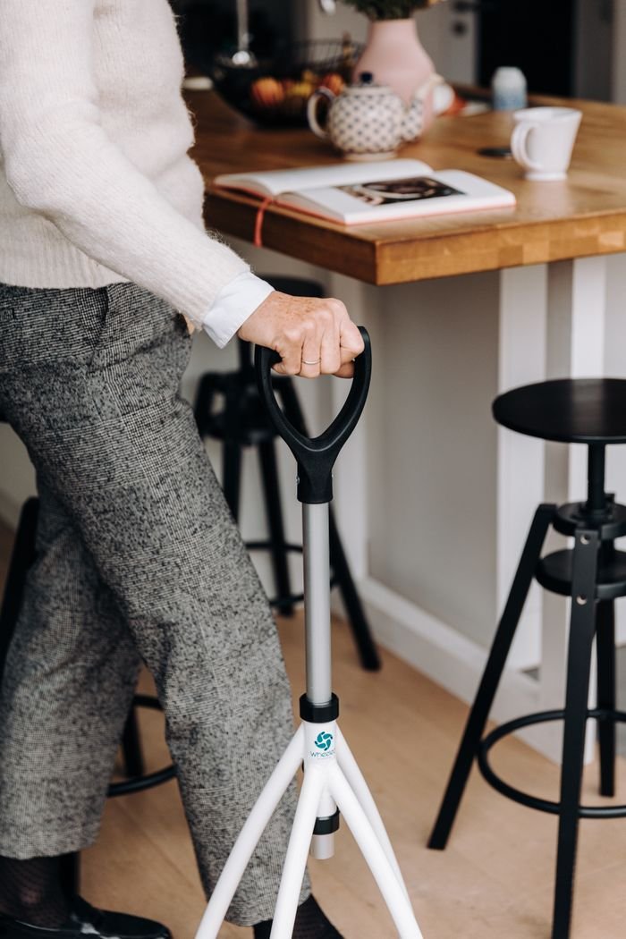 who-we-are A senior adult using a walking cane in a modern kitchen setting, promoting independence and mobility.