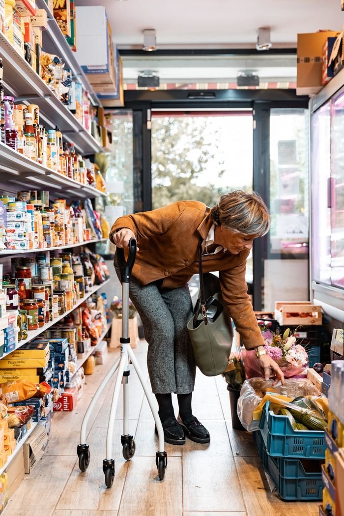 about-us A senior woman with a rollator shopping for produce in a grocery store aisle.