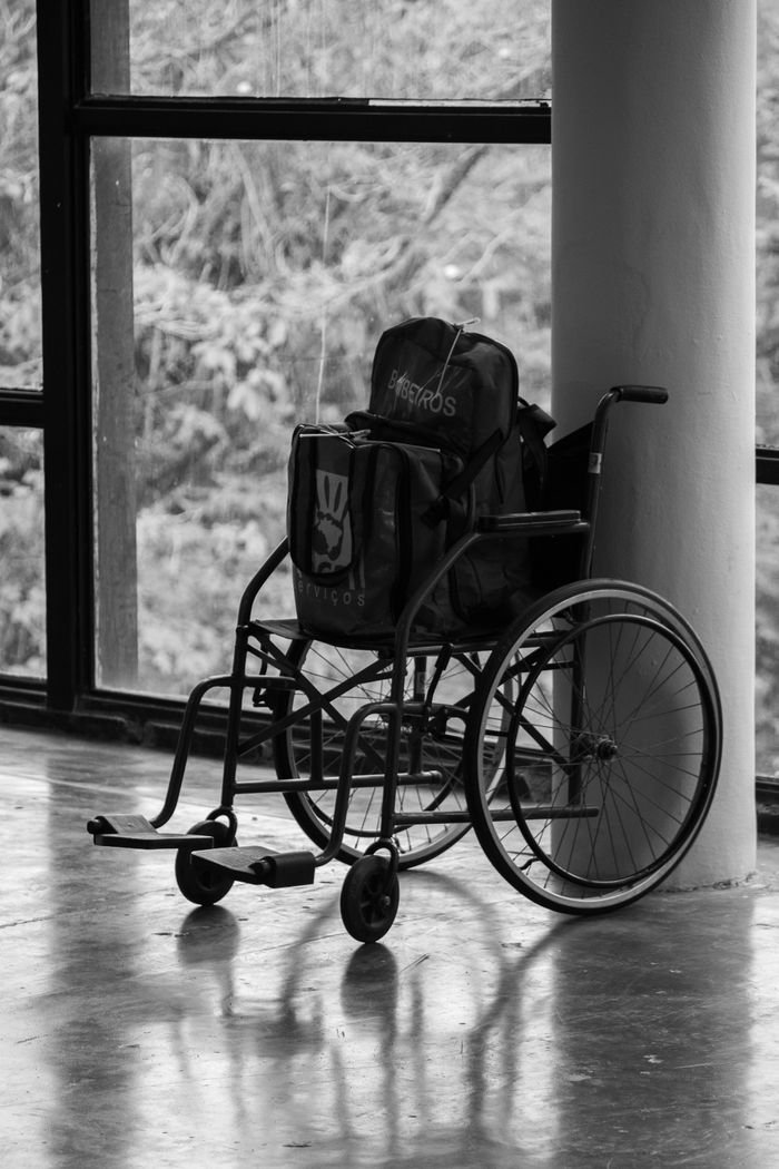our-story Black and white image of an empty wheelchair by a window, conveying solitude.